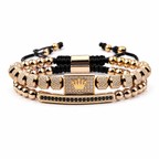 Gold and black beaded bracelets with a crown charm on a white background. Exokeleton Royale Bracelet