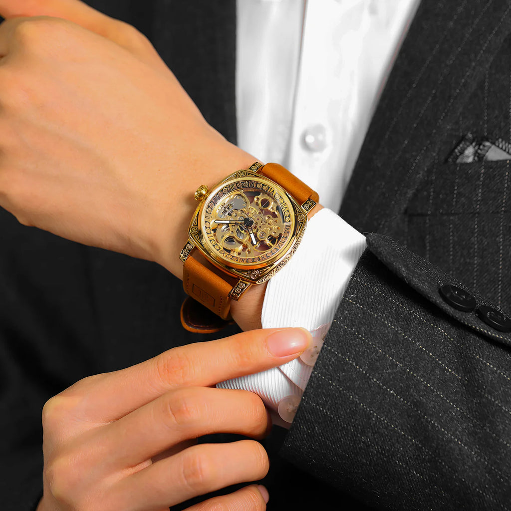 Person wearing a gold wristwatch with a brown leather strap on a suit sleeve.