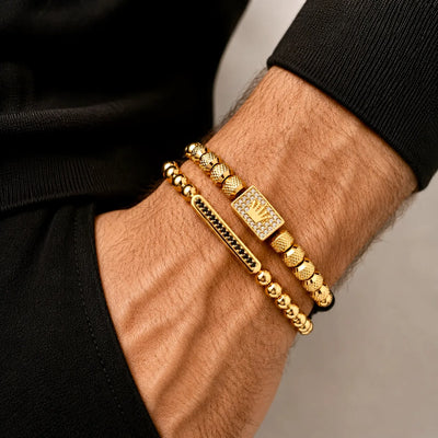 Gold Royale bracelets on a person's wrist with a neutral background. Gold and black beaded bracelets with a crown charm on a white background. Exokeleton Royale Bracelet